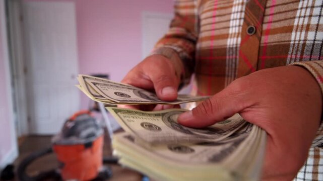 A man meticulously counts dollar bills to budget for home renovation materials. His focused expression reveals the importance of this task in a warm, inviting space