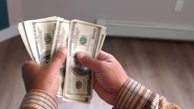A man carefully tallies his dollar bills to calculate the expenses needed for his home renovation project, focusing on essential materials