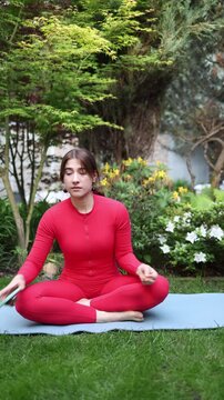 Vertical screen Woman sits in lotus pose outdoors trying to meditate but keeps reacting to smartphone showing strong digital addiction and inability to stay offline
