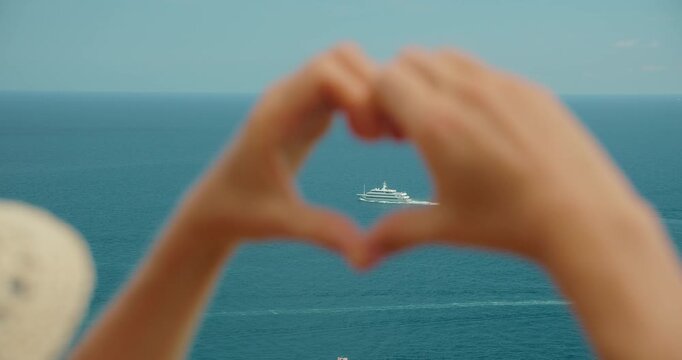 Hands form a heart around a yacht on the blue Mediterranean summer sea