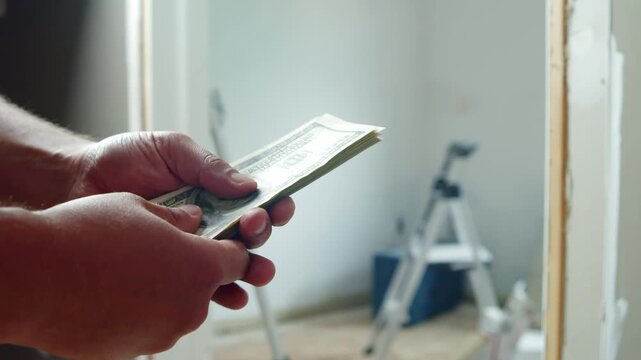 A man carefully counts dollar bills as he prepares for home renovation. He thoughtfully assesses how much money he needs for materials to transform his space