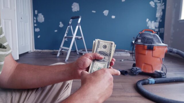 A man carefully counts dollar bills to determine the budget for materials necessary to renovate his home. This moment highlights his dedication and thoughtfulness