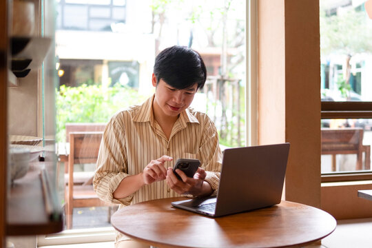 A young man is typing a message on his cell phone at a wooden table in a cozy coffee shop.