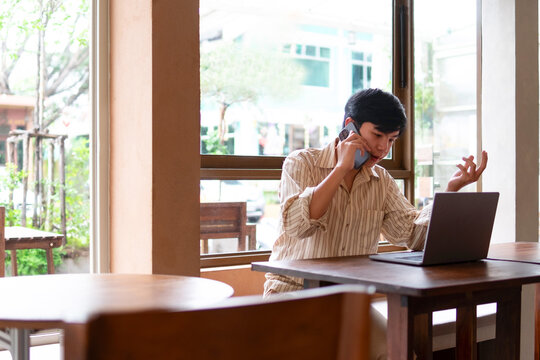 A young man is talking on his cell phone at a wooden table in a cozy coffee shop.