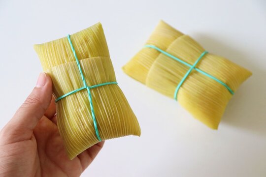 Female hand holding a traditional Brazilian pamonha wrapped in corn husk. Typical food of Brazilian Sao Joao parties.