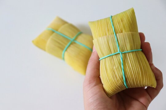Female hand holding a traditional Brazilian pamonha wrapped in corn husk. Typical food of Brazilian Sao Joao parties.