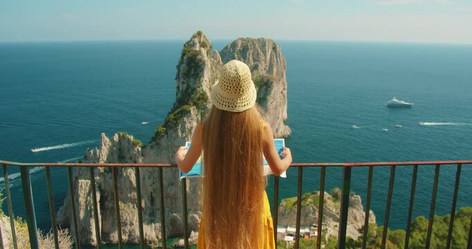 Tourist woman studying a coastal map above the Faraglioni rocks in Capri on a summer day
