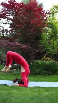 Vertical screen Woman practices deep inversion with strong back arch on forearms in the garden highlighting risk of injury when performing extreme yoga poses without supervision