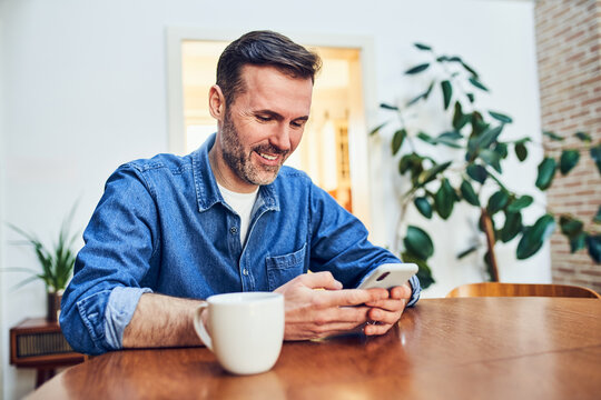 Man smiling at smartphone at dining table at home