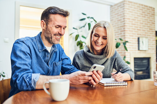 Couple looking at smartphone together at home dining table