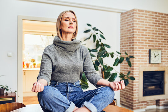 Woman meditating in lotus pose in cozy living room at home sitting on a table