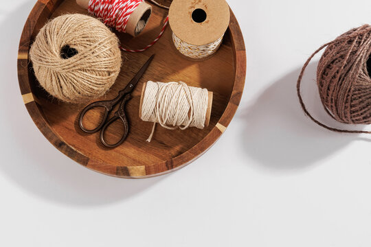 Rustic craft workspace with natural twine balls, cotton string spools and scissors in wooden tray on light background, diy craft and eco packaging supplies concept
