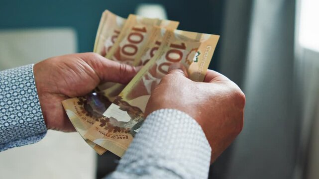 A man carefully counts Canadian dollar bills in a calm and cozy room, showcasing the texture and details of the currency as he organizes the notes with precision
