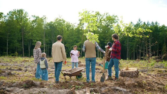 Volunteer coordinator briefing community members before environmental restoration work on deforested land. Group discussing tree planting strategy and preparing tools for reforestation project.