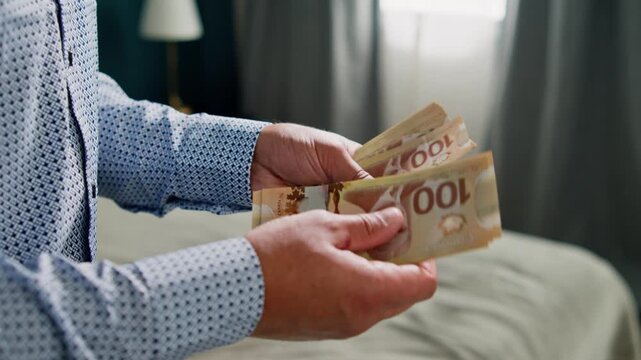 Close-up of a man's hands as he meticulously counts Canadian dollar bills in a warm, inviting room, capturing the essence of financial dealings and careful attention