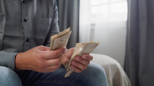 A man meticulously counts Canadian dollars in a warm and inviting room. Each bill is examined with care, revealing the importance of the task at hand