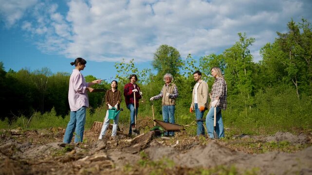 Group of volunteers listening to project coordinator before starting tree planting activities. Community members preparing reforestation work on cleared land. Environmental restoration initiative.