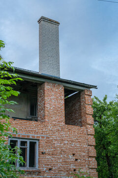 a weathered, partially ruined brick building featuring prominent corner quoins and an upright chimney against a cloudy sky.