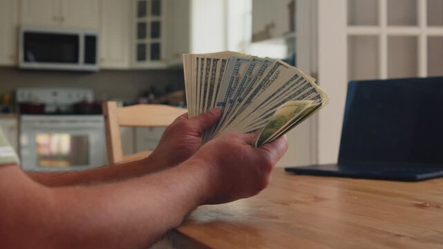 In a warm kitchen, a man focuses on counting a stack of dollar bills. His calm demeanor illustrates the satisfaction of handling his finances privately