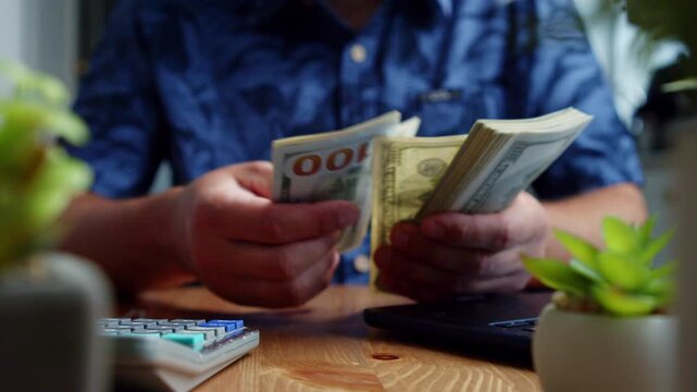 A man sits comfortably at his table, carefully counting U.S. dollar bills with focus and precision. The room is filled with a sense of tranquility and purpose