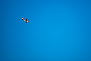 Fototapeta premium Red and white sport airplane flying high in the clear blue sky, minimalist aviation background with vast copy space for text, remote controlled RC plane flight.