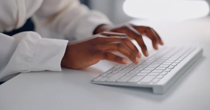 Hands of black female professional typing on modern white keyboard in bright office space.