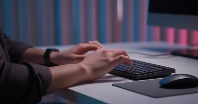 Hands on keyboard typing at modern computer workstation with colorful background in slow motion.