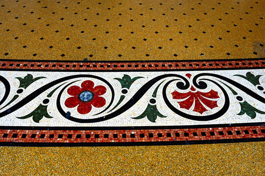 colorful yellow and black shiny terrazzo floor with ceramic mosaic inlay. flower pattern. worn repaired surface. covered exterior corridor in genoa, italy. art, architecture and travel concept.