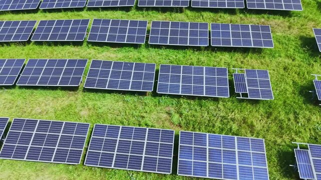 Close aerial view solar panel rows forming geometric patterns over green grass, detailed reflective cells and mounting frames, service tracks and grazing