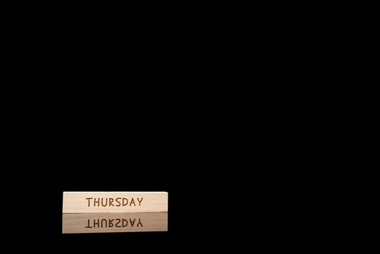 Wooden block with the word &ldquo;THURSDAY&rdquo; on a dark reflective background with large copy space, symbolizing planning, scheduling, productivity and weekly routine.