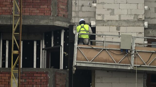 A construction worker installs exterior facade panels on a modern building
