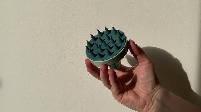 Plastic massager for hair and scalp in a woman's hand on a white background. Hair care. Blue-green massager. Silicone hair brush. 4k