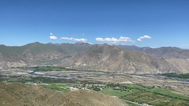 Panoramic view of Kyi Chu Valley winding through mountains near Ganden Monastery, Lhasa, Tibet, with lush green farmland in summer.