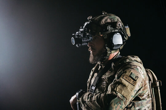 Man soldier in side profile wearing night vision device and tactical headset under studio light, military surveillance, night mission concept. Modern special operations. Free copy space