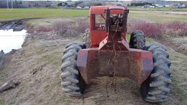 Drone footage of a rusty Timberjack skidder parked beside a stream, highlighting worn tires, chains, and the rugged character of the forestry industry.