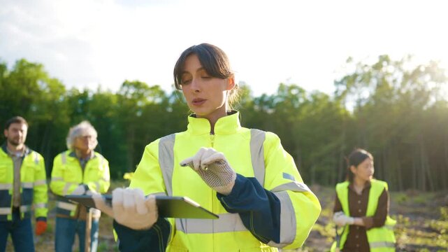 Female environmental coordinator giving instructions to volunteer team at reforestation site. Woman managing forest restoration project after logging. Ecology conservation and sustainable recovery.