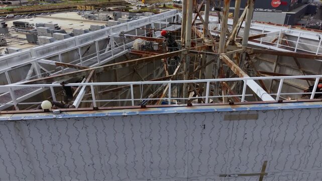 High-angle view of maintenance work with workers on a rusted steel structure above a multi-lane roadway. Rope access and working at height technicians seen at a job site.