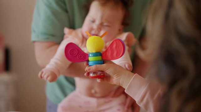A baby lies comfortably while watching a colorful toy, and doing mobility exercises with a caregiver