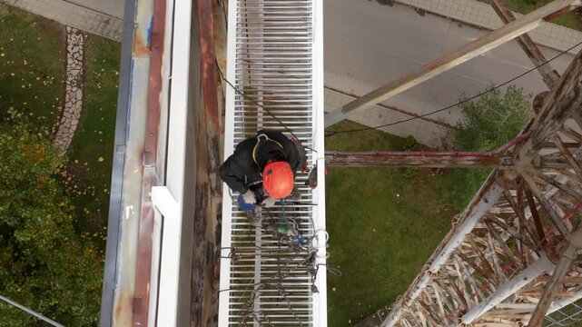 Aerial drone footage of certified rope access technicians performing inspection and maintenance work on a large steel industrial structure at height. Workers wearing personal protective equipment and 
