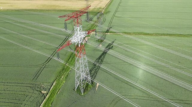vue a&eacute;rienne d'un pyl&ocirc;ne &eacute;lectrique haute tension. La structure m&eacute;tallique est peinte en rouge et blanc, sur un fond vert de champs Les c&acirc;bles &eacute;lectriques sont bien visibles.