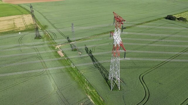 vue a&eacute;rienne d'un pyl&ocirc;ne &eacute;lectrique haute tension. La structure m&eacute;tallique est peinte en rouge et blanc, sur un fond vert de champs Les c&acirc;bles &eacute;lectriques sont bien visibles.
