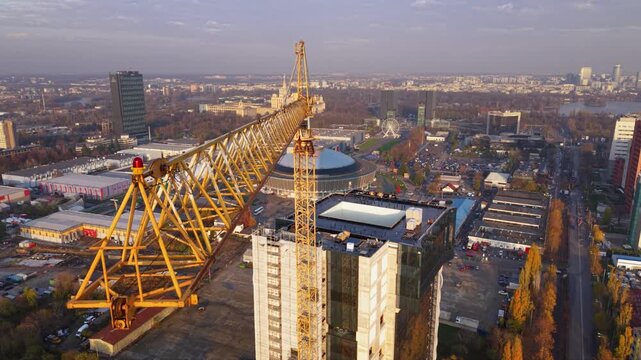 Aerial drone footage of a tower crane operating above a modern high-rise construction site with a panoramic city skyline in the background. The scene showcases urban development, commercial real estat