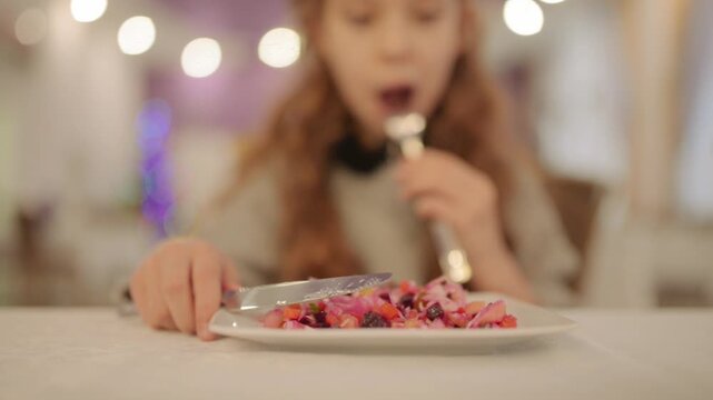 Beautiful teen girl using fork and knife eats salad vinaigrette