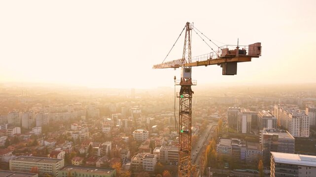Aerial drone footage of a tower crane operating above a modern high-rise construction site with a panoramic city skyline in the background. The scene showcases urban development, commercial real estat