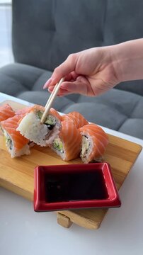 A classic Philadelphia roll wrapped with fresh salmon is gently dipped into dark soy sauce served in a red rectangular dipping dish