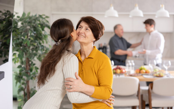 Friendly mother-in-law greeting visiting young daughter-in-law with tender kiss, embodying warm welcome in comfy home setting. Intergenerational family bonding concept..