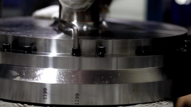 ​A technical worker uses a hex wrench tool to loosen a steel bolt on a circular metallic industrial component.