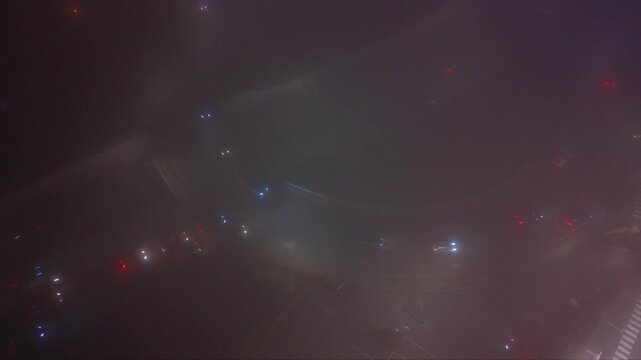 Nighttime underpass or trench-style highway with light traffic, viewed from above in foggy low-light conditions