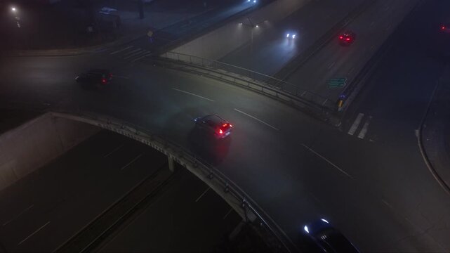 Nighttime underpass or trench-style highway with light traffic, viewed from above in foggy low-light conditions