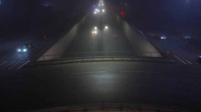Nighttime underpass or trench-style highway with light traffic, viewed from above in foggy low-light conditions